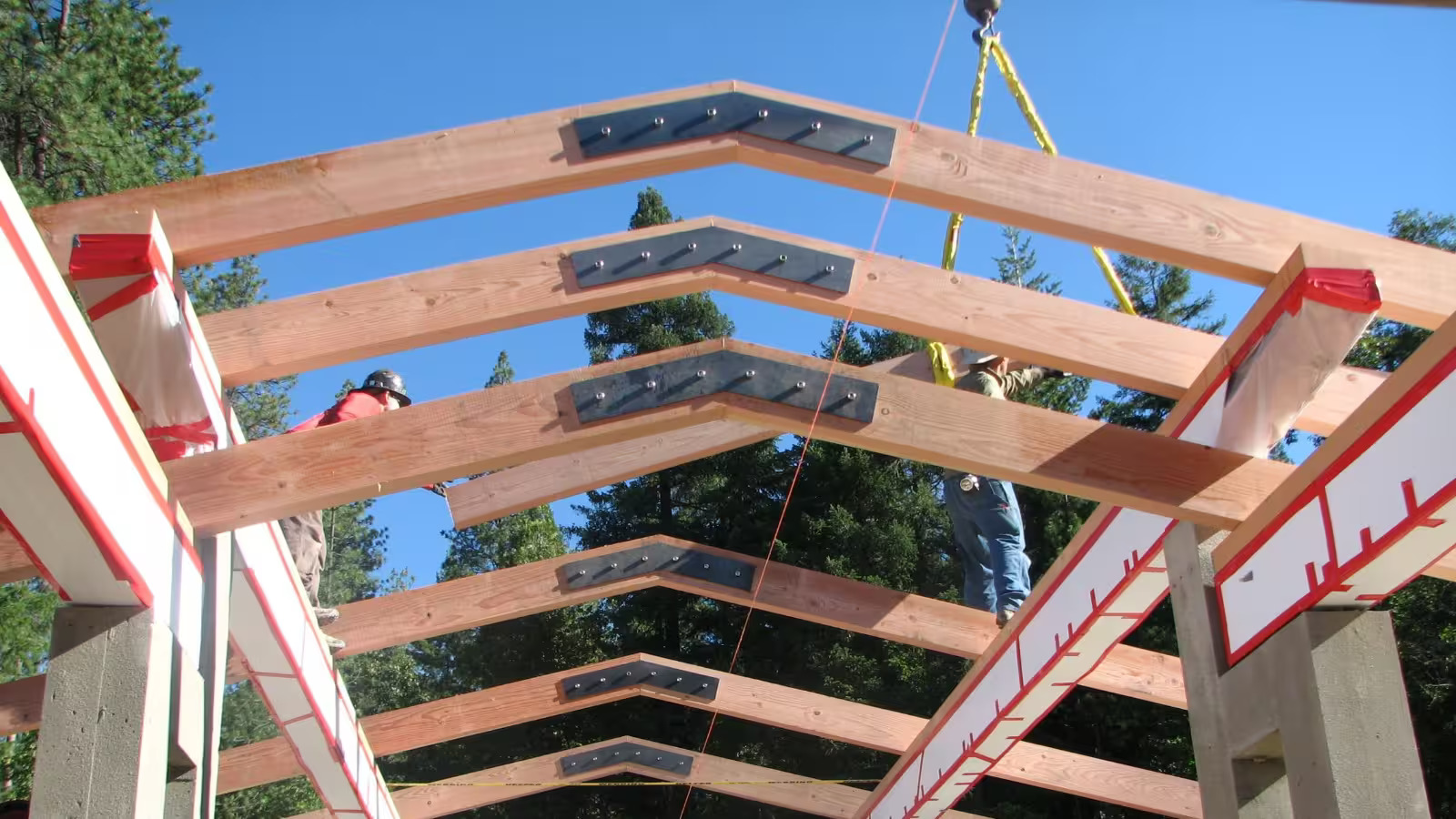 NC Builders crew framing a heavy-timber roof on a new home under a clear sky