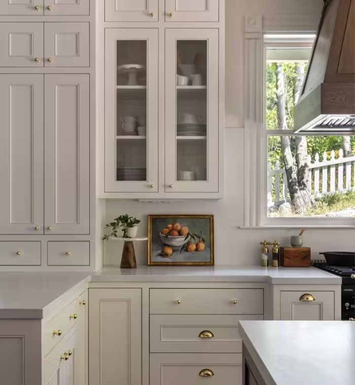 Custom kitchen cabinetry with glass-front upper cabinets, brass cup pulls, and a window to the garden