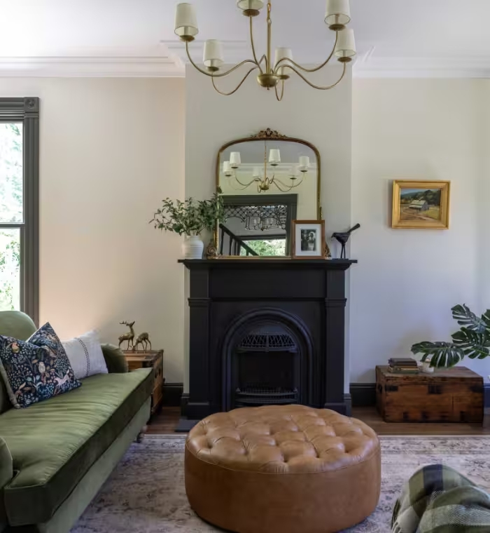 Living room with a restored cast-iron fireplace, ornate plaster ceiling medallion, and a green velvet sofa