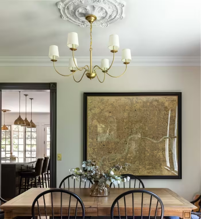 Dining room with a wood table and spindle-back chairs beneath a brass chandelier and a large framed antique map