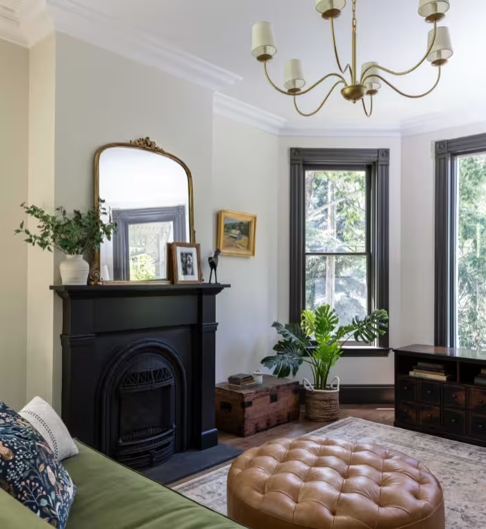 Sitting room with a cast-iron fireplace, gilt mirror, and tall windows trimmed in dark green