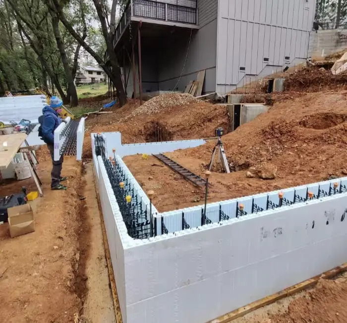 Stacked insulated concrete forms set as foundation walls on a sloped, wooded building site