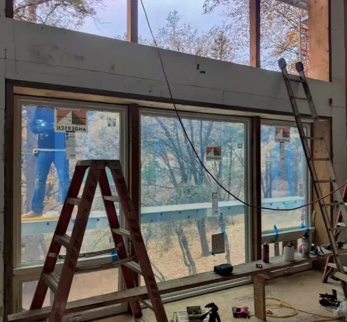 Row of large windows set in an insulated-concrete wall, framing autumn oaks during construction