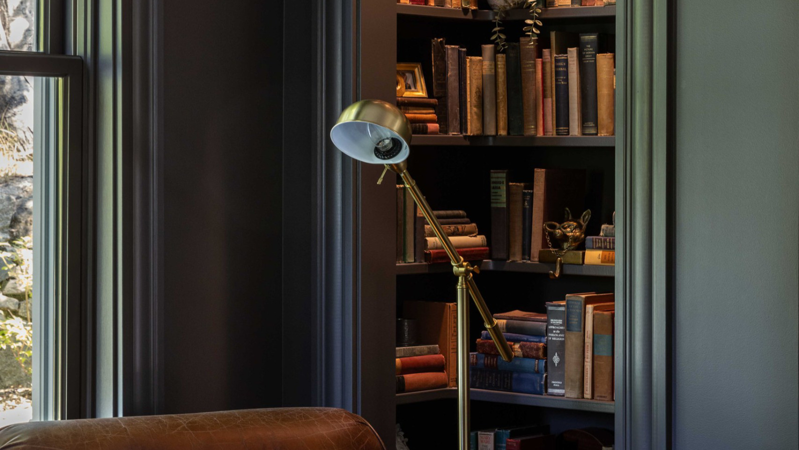 Dark green library nook with built-in bookshelves and a brass reading lamp inside a renovated historic home