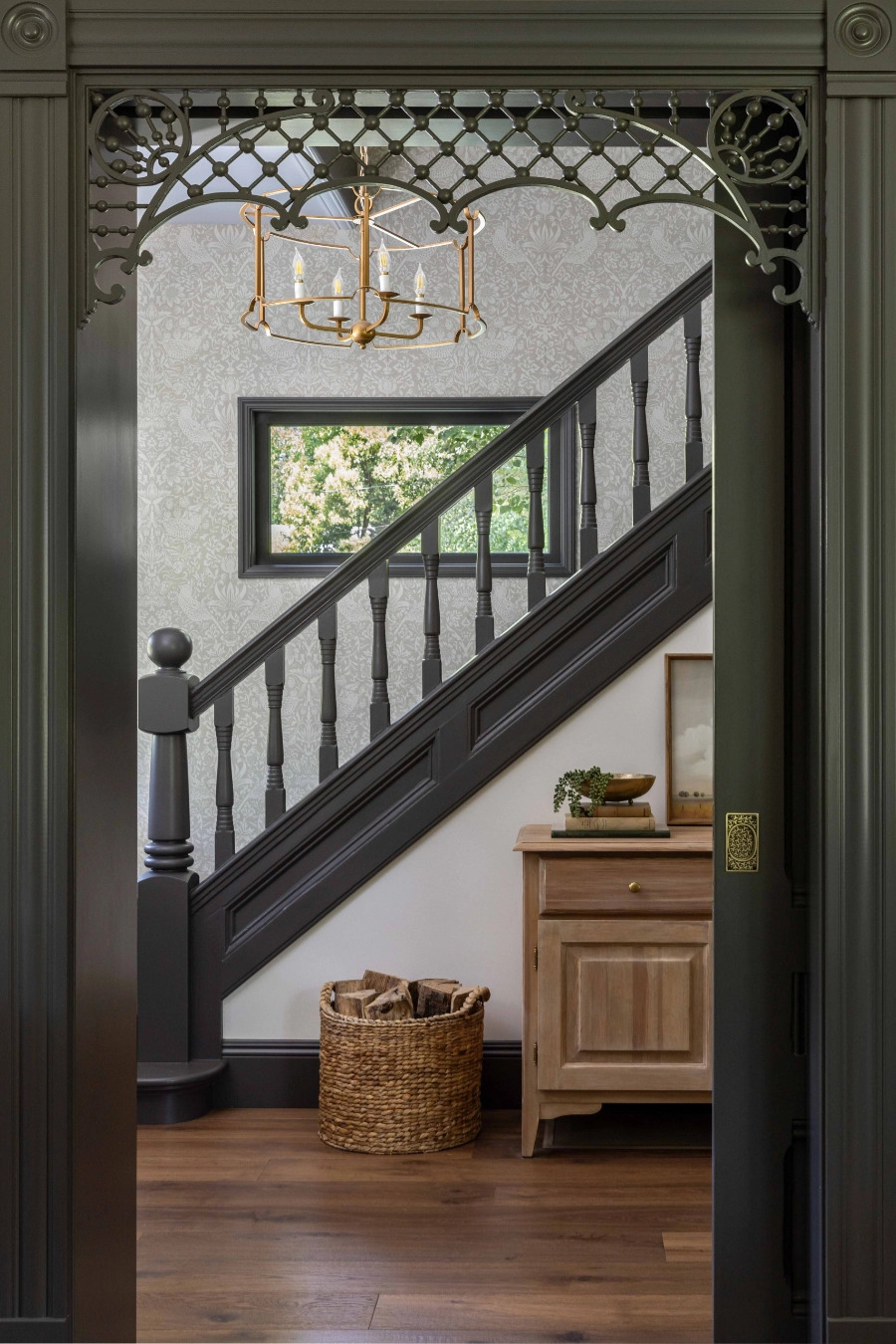Carved fretwork archway framing a restored Victorian staircase with dark spindle railings and patterned wallpaper