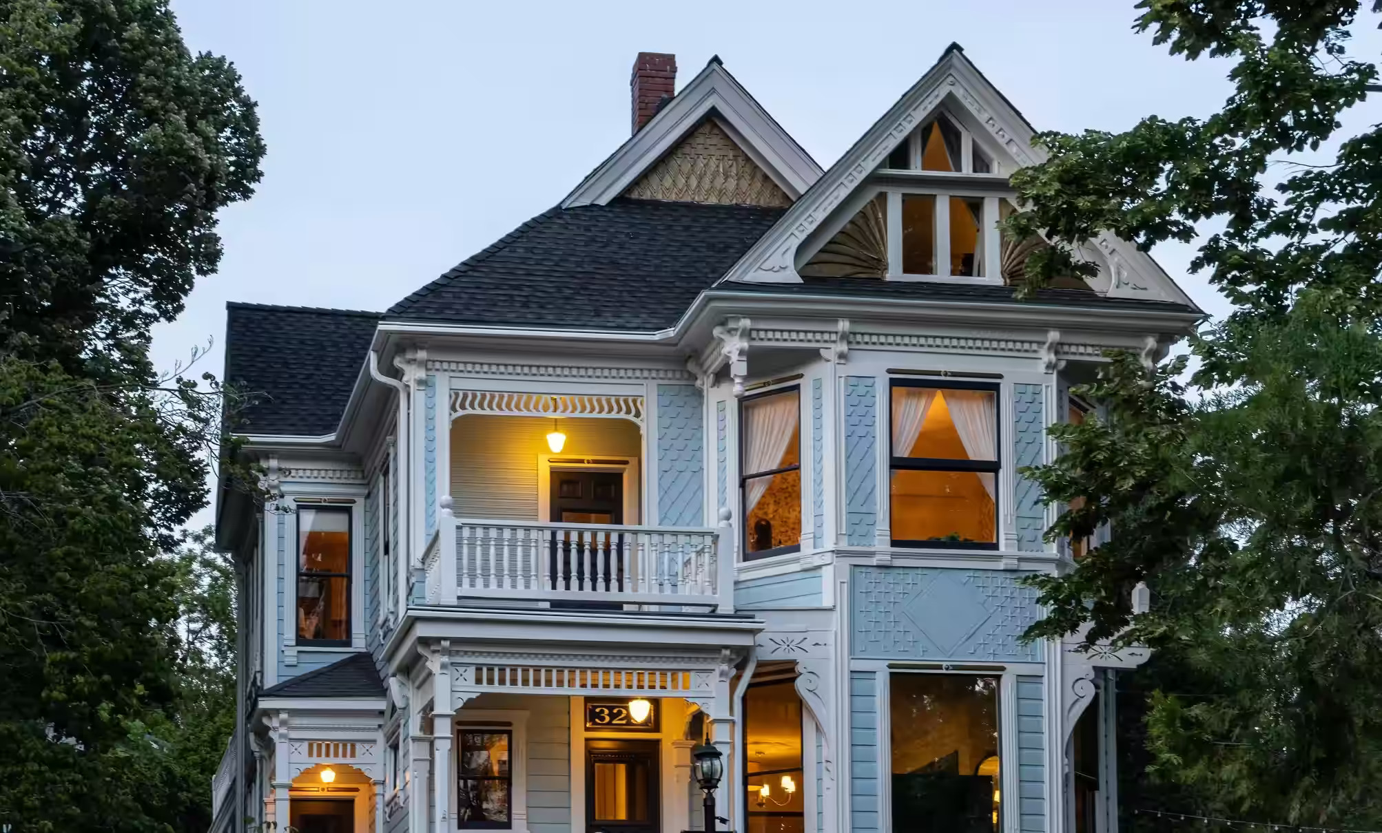 Restored blue-and-white Victorian home in Nevada City at twilight, warmly lit behind a white picket fence