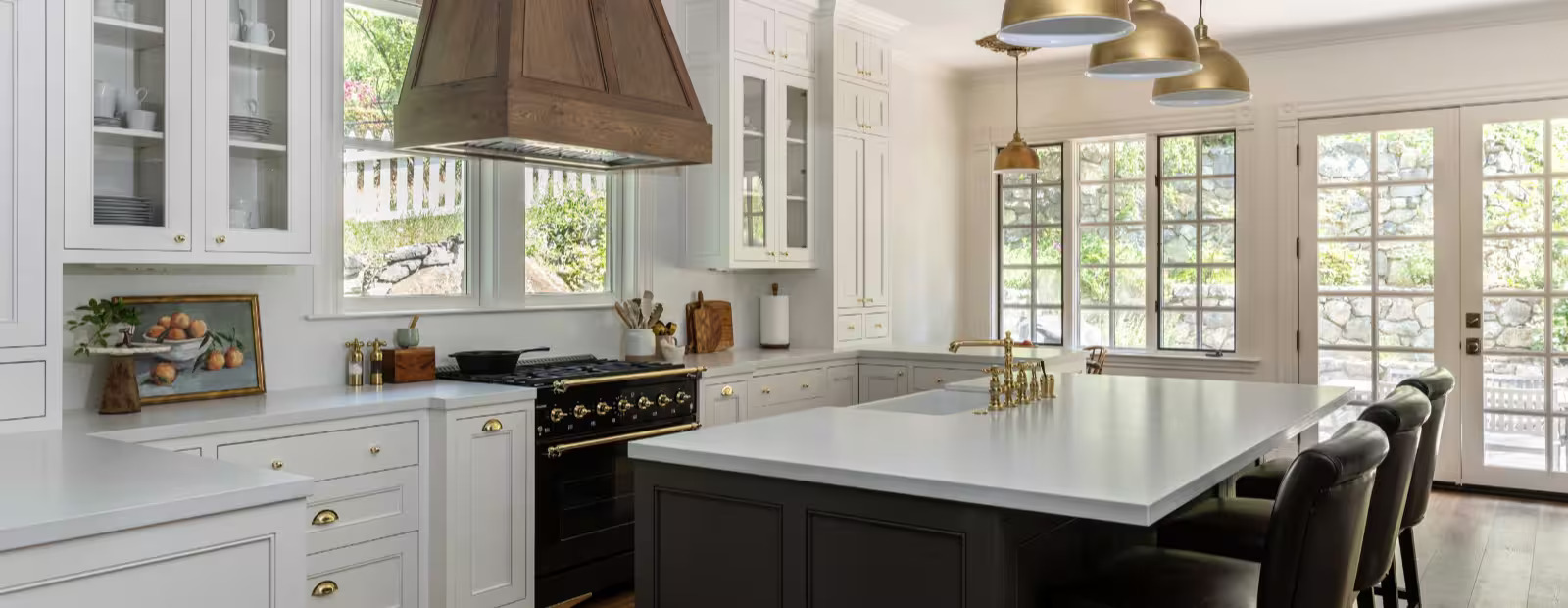 Remodeled kitchen with white cabinetry, a custom wood range hood, and a large island under brass pendant lights