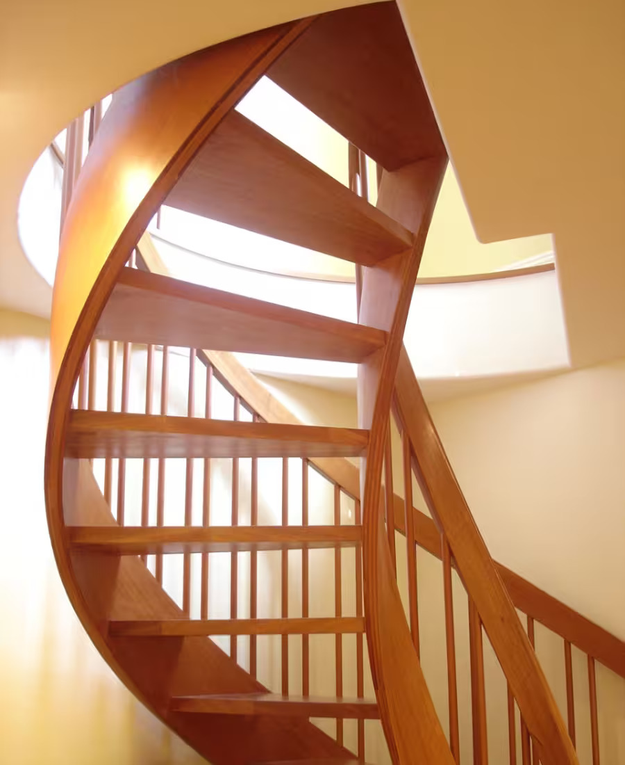 Custom curved wood staircase with slender balusters rising toward a skylit landing.